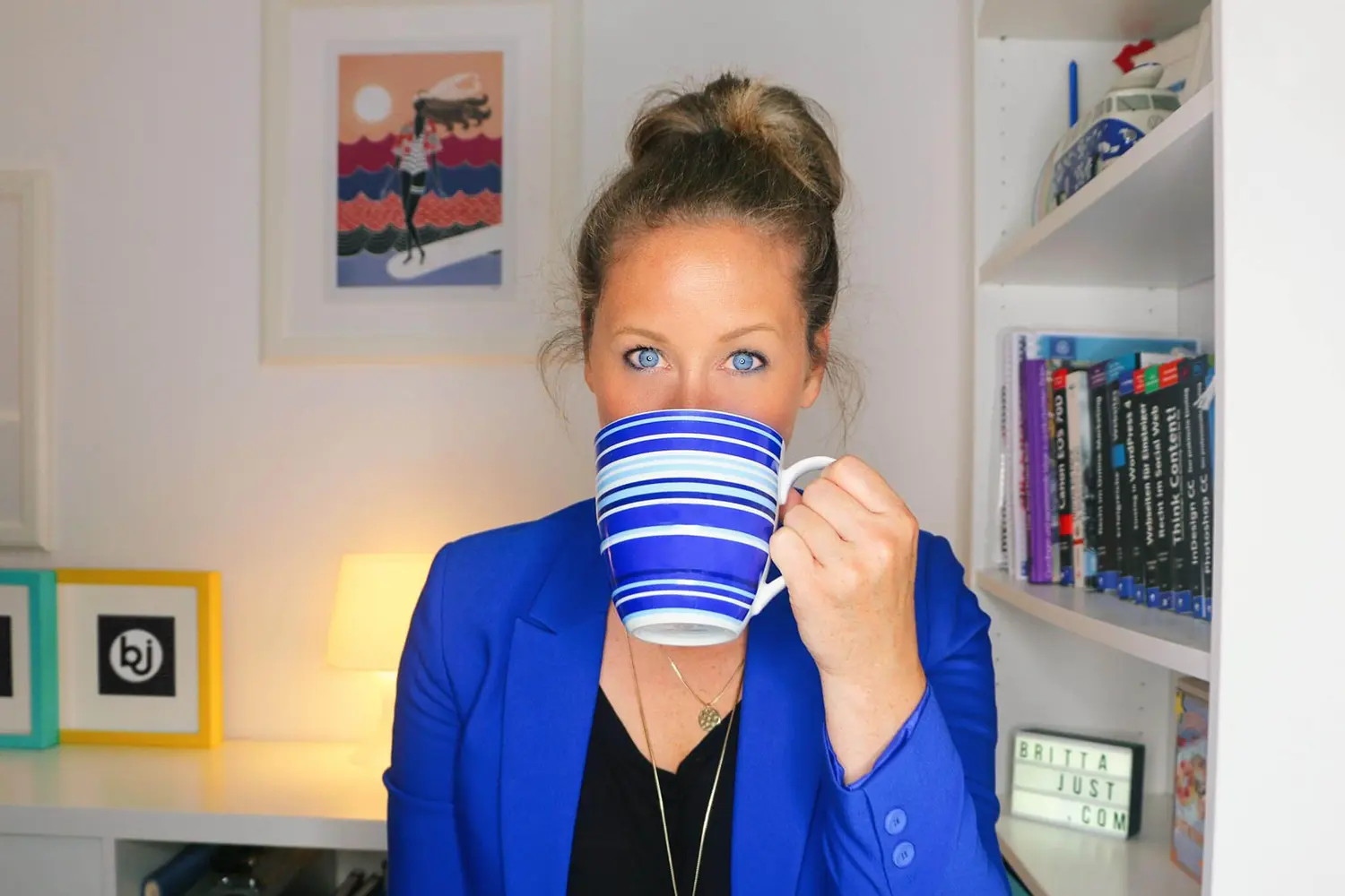 Britta Just in a blue blazer, holding her blue striped coffee mug whilst giving away 50 fun facts about herself.