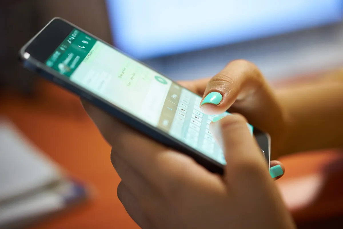Zwei Hände, die ein Smartphone halten und eine Nachricht via WhatsApp tippen.