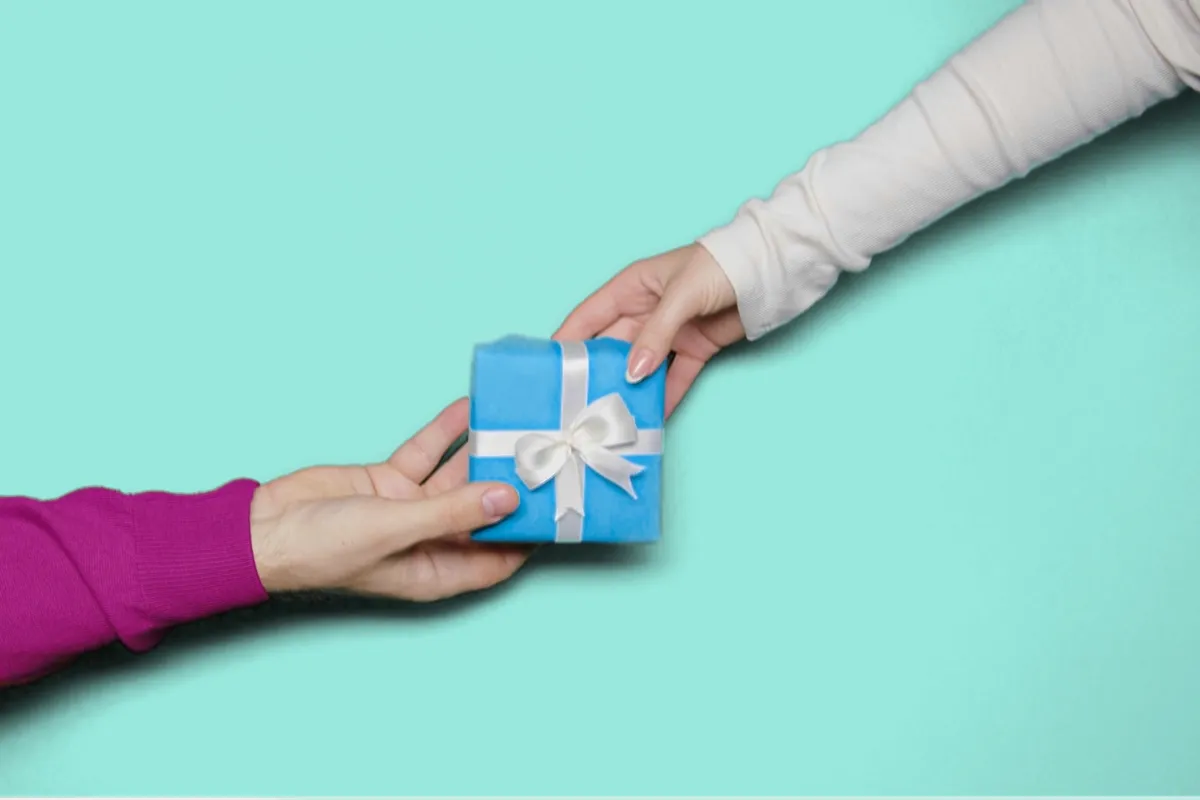 Eine Hand reicht einer anderen Hand ein kleines Geschenk als Symbol für Adventskalender als Lead Magnet.