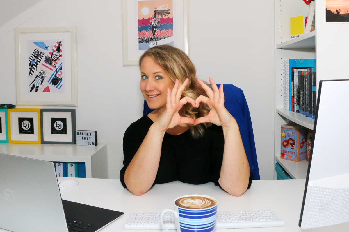 Britta sitzt an ihrem Schreibtisch und formt ein Herz mit den Händen, während sie die harte Wahrheit liefert: 5 Zeichen, woran ich sofort erkenne, dass Deine Website potenzielle Kund:innen vergrault – und wie Du das änderst.